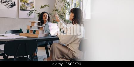 Due donne professionisti si impegnano in una discussione sulla gestione dei progetti in un ufficio contemporaneo. Si concentrano sulla strategia e sul lavoro di squadra. Foto Stock