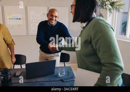 Due professionisti si salutano con una stretta di mano durante una riunione collaborativa in un ufficio, mostrando il lavoro di squadra e la comunicazione. Foto Stock