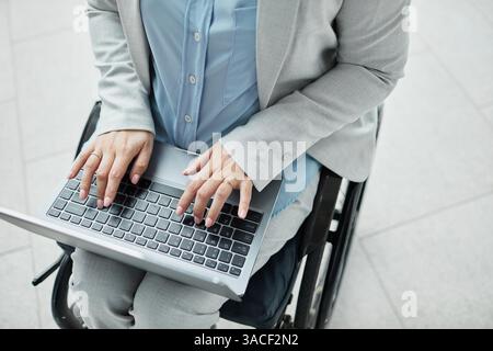 Primo piano minimale di una donna d'affari irriconoscibile in sedia a rotelle che utilizza laptop e spazio per copiare Foto Stock