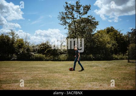 Ragazzo che calcia la palla da calcio sul campo. Foto Stock