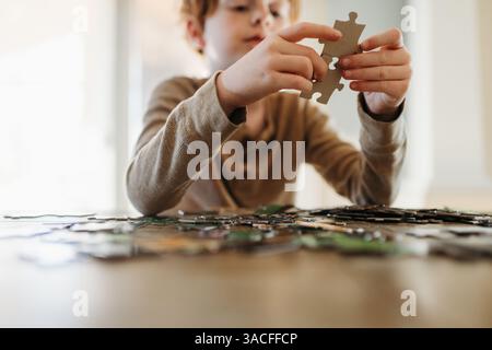 Ragazzo che mette insieme pezzi di puzzle a casa al tavolo della cucina Foto Stock
