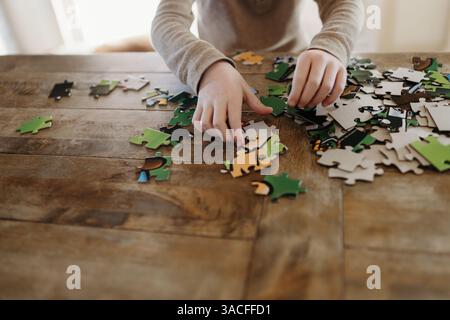 Primo piano di mani che mettono insieme il puzzle al tavolo della cucina a casa Foto Stock