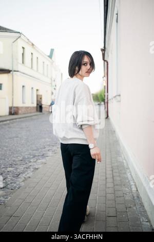 Donna elegante con una felpa leggera che percorre una tranquilla strada della città Foto Stock