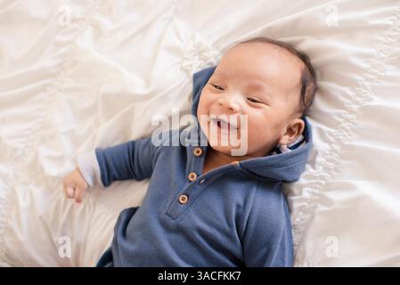 Bambino sorridente disteso su soffici letti bianchi con cappuccio blu Foto Stock