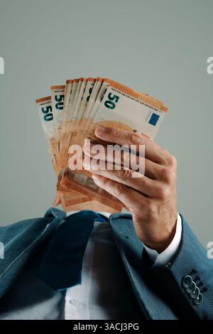 un uomo d'affari, indossando un elegante abito blu, ha in mano alcune banconote in euro, viste dal basso Foto Stock