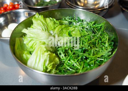 Ciotola riempita con lattuga verde croccante e foglie di rucola da sciacquare, pronta per la preparazione dell'insalata in cucina. Foto Stock