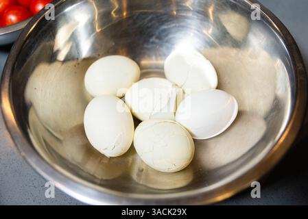 Sei uova sode con gusci incrinati collocate in un recipiente di miscelazione in acciaio inossidabile su un piano di lavoro della cucina. Foto Stock