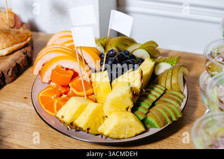 Vivace assortimento di frutta fresca a fette, tra cui ananas, kiwi, pera, uva e agrumi su un piatto da portata in occasione di un evento. Foto Stock