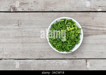 Ciotola bianca con erba cipollina tritata su sfondo di legno chiaro Foto Stock