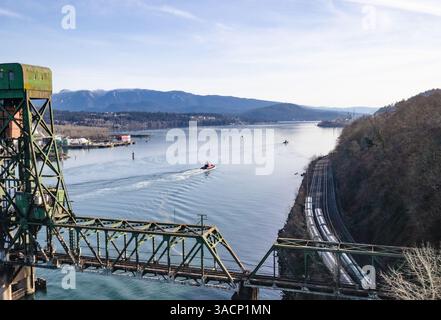 Ponte ferroviario sul fiume o sull'insenatura con rimorchiatori, treno ferroviario cargo e costa industriale. Panorama dei trasporti marittimi. Second Narrows, Inner Harbour, Foto Stock