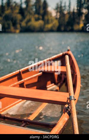 Primo piano del lago autunnale con barche di legno rosse che galleggiano su acque calme, effetto sfocato, circondato da verde pineta, tranquillo paesaggio stagionale Foto Stock