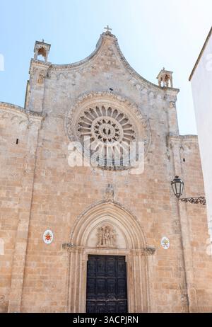 La facciata della cattedrale di Ostuni mostra la sua intricata rosetta, il portale ad arco e dettagli architettonici, inondati dalla luce del sole Foto Stock
