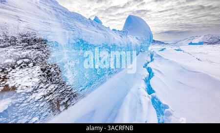 Un crepaccio si apre nel ghiaccio di fronte a iceberg e montagne intorno alla costa dell'isola di Baffin in primavera Foto Stock