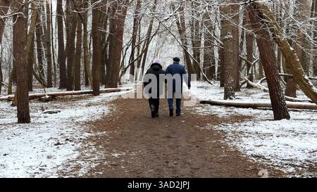 Coppia matura che va su un sentiero innevato nella pineta invernale. Marito anziano e moglie camminano attraverso il sentiero nel bosco di conifere. Coppia più vecchia di Foto Stock