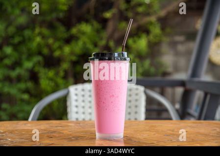 Il latte dolce rosa freddo in stile thailandese è una bevanda a base di latte mescolata con acqua dolce rossa in vetro con paglia su un tavolo di legno nel caffè o nel caffè ristorante blu Foto Stock