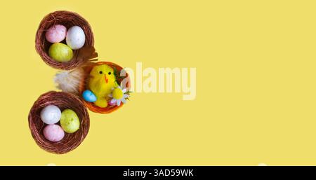 Ci sono un sacco di uova di Pasqua e un pollo giocattolo nei nidi su sfondo giallo. Concetto di Pasqua, primo piano. Foto Stock
