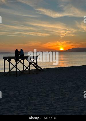Una coppia si è seduta su una piattaforma di bagnino sulla spiaggia a guardare il tramonto sulla baia di Palma, sull'isola di Maiorca, in Spagna Foto Stock