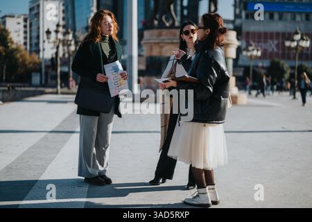 Tre giovani donne si impegnano in una discussione collaborativa all'aperto. Analizzano i piani di progetto e definiscono strategie per lo sviluppo aziendale. Foto Stock