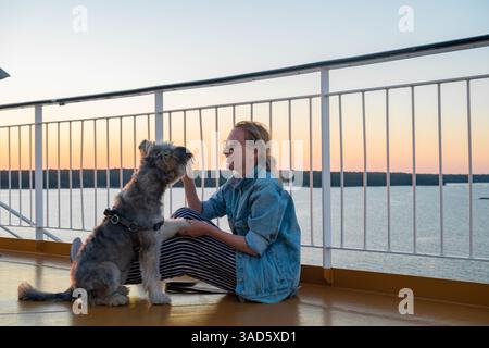 Giovane donna seduta sul ponte di una nave da crociera con il suo cane Foto Stock