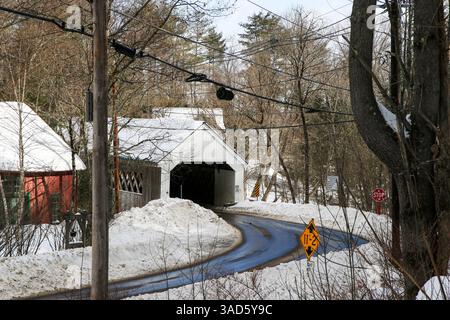 La neve copre il terreno mentre una strada tortuosa si avvicina a un affascinante ponte coperto. Foto Stock