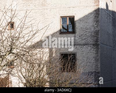 La luce del sole proietta intricate ombre da una finestra sulla parete testurizzata di un edificio a Gothenburg. I rami senza foglie aggiungono un tocco di bellezza alla sc Foto Stock