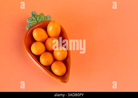 Piatto minimalista stagionale con uova di cioccolato bilanciate all'interno di un piatto di carote in ceramica Foto Stock