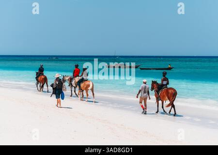 Zanzibar, 01.01.2024: Tour a cavallo su una spiaggia tropicale con guide e turisti che si godono il paesaggio Foto Stock