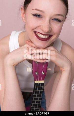 Ritratto di una giovane musicista con ukulele. Bella donna di 18 anni con un sorriso grosso e toothy, atteggiamento positivo ed espressione gioiosa. E' la testa Foto Stock