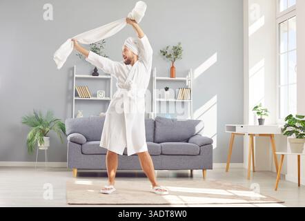 Uomo felice e divertente in un accappatoio e asciugamano bianco, che si rilassa e si diverte dopo la doccia Foto Stock