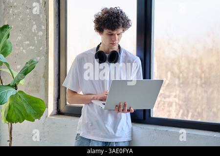 Ritrarre un bel giovane maschio usando un laptop in piedi vicino alla finestra Foto Stock
