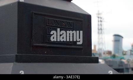 Londra, Regno Unito - 16 dicembre 2023: Targa su un pilastro di pietra adiacente al fiume Tamigi che indica London Bridge City con la HMS Belfast sullo sfondo Foto Stock