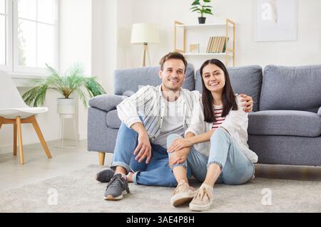 Una giovane coppia sorridente seduto su un morbido tappeto nel soggiorno, rilassandosi e godendosi momenti insieme. Foto Stock