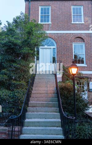 Un'alta scala in cemento che conduce ad una porta bianca su un edificio in mattoni durante l'ora blu Foto Stock