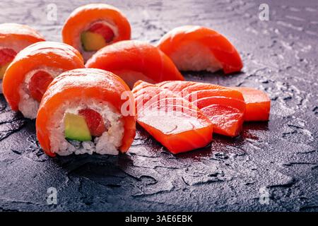 Set di sushi con uramaki di salmone, fette di sashimi e nigiri su sfondo di ardesia nera, con spazio di copia Foto Stock