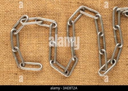 Un pezzo di catena metallica su tessuto di iuta, macro, vista dall'alto. Foto Stock