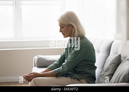 Una donna anziana triste seduta da sola sul divano soffre di depressione Foto Stock