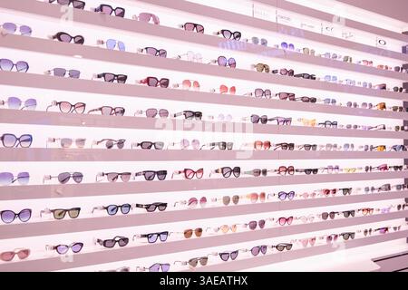 Una fila di occhiali in esposizione in un negozio. Gli occhiali sono di vari colori e stili, tra cui occhiali da sole e montature Cat-eye. Il display è organo Foto Stock