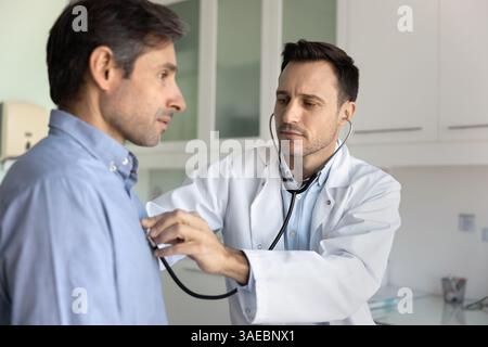 Cardiologo che utilizza lo stetoscopio per ascoltare il battito cardiaco del paziente maschile Foto Stock