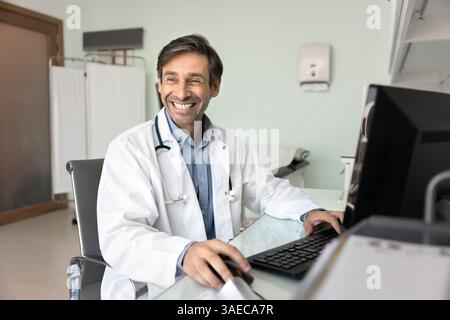 Terapista ridendo seduto alla scrivania e lavorando al computer Foto Stock