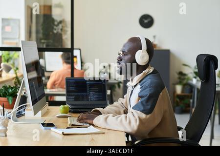 Giovane designer serio con cuffie sedute sul posto di lavoro davanti allo schermo del computer desktop con un modello di linguaggio visivo Foto Stock