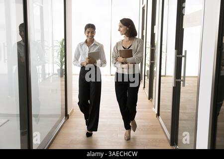 Due colleghi multirazziali che camminano e parlano nel moderno corridoio dell'ufficio Foto Stock