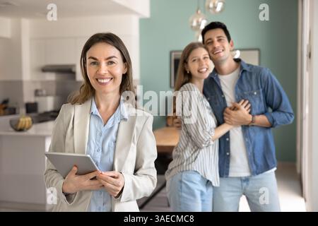 Agente immobiliare in piedi al coperto con felice soddisfatto giovane coppia Foto Stock