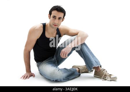 Bellissimo ragazzo caucasico con canotta nera e jeans seduti sul pavimento, isolato, New York, USA, Nord America Foto Stock