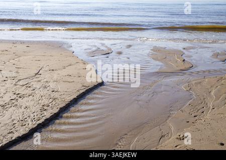 Onde delicate che scivolano sulla spiaggia di sabbia creando piccoli ruscelli d'acqua Foto Stock