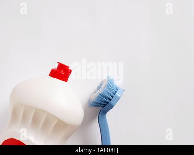 Spazzola per piatti blu e flacone bianco con detergente per tappo rosso su sfondo bianco con spazio di copia Foto Stock