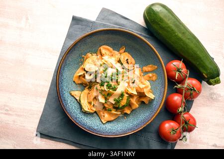 Tagliatelle di pasta con zucchine in salsa di pomodoro, parmigiano e erba cipollina guarnire in un piatto blu su un tavolo di legno chiaro, spazio copia, angolo alto vi Foto Stock