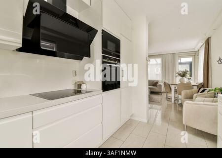 Una cucina luminosa e contemporanea con eleganti mobili, elettrodomestici integrati e un'invitante area pranzo che esalta l'estetica generale. Foto Stock
