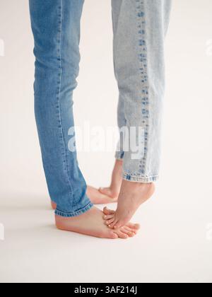 Primo piano di una coppia romantica di uomini e donne a piedi nudi in jeans, che abbracciano e si baciano delicatamente sullo sfondo chiaro. momen intima e tenera Foto Stock
