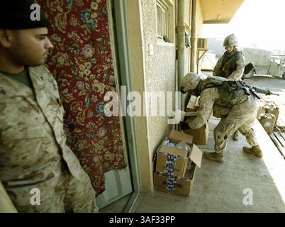 21 dicembre 2004; Fallujah, Iraq; A Marine with 1st Battalion, 3rd Marines, guarda come il tenente ALEXANDRIA S. PLUCINSKI e Lance Cpl. JACOB M. WEATHERBY, entrambi parte di un convoglio Combat Service Support Company 115, consegnano pacchetti di assistenza al centro operativo logistico 1/3 a Fallujah, Iraq, 21 dicembre 2004. L'unità di Camp Pendleton, California, facente parte del 1st Force Service Support Group, è responsabile della fornitura di provviste, come cibo, acqua, munizioni e carburante, alle unità marine che operano a Fallujah e nelle sue vicinanze. A novembre, il CSSC-115 di Camp Pendleton, California, ha registrato più di 31.000 unità Foto Stock