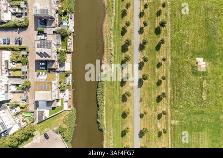 Questa immagine mostra una vista aerea di una moderna area urbana adiacente a un fiume, con edifici, parchi e sentieri fiancheggiati da alberi. Foto Stock